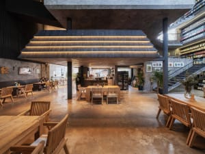 Well-lit industrial-style café interior with concrete flooring, wooden furniture, and bookshelves.