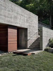 A modern house with concrete exterior featuring a wooden door and a staircase leading up to it.