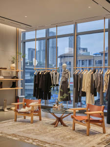 A modern retail store display featuring a curation of clothing and accessories arranged on a glass table surrounded by wooden