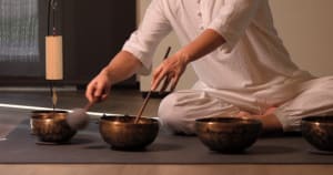 A person is seen using wooden mallets to strike metal bowls in a music therapy setting.
