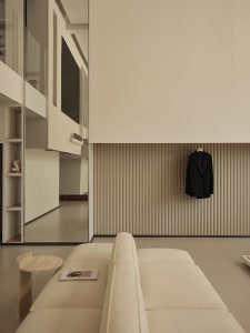 A minimalist living room with neutral-toned furniture and a black blazer hanging on the wall.