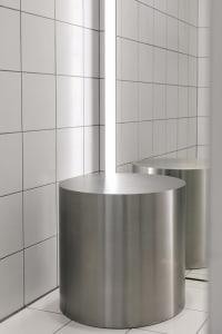 Modern minimalist bathroom featuring cylindrical metal stools on a white tiled floor and wall.
