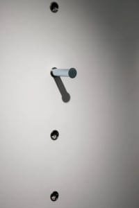 A metal lock with a gray cylinder handle attached to a smooth, white surface.