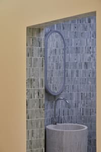 Modern minimalist bathroom featuring marble tiles and a cylindrical sink.