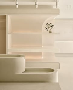 A modern minimalist library with minimalist white shelves made of plaster, light-colored wooden floors and a white curtain.