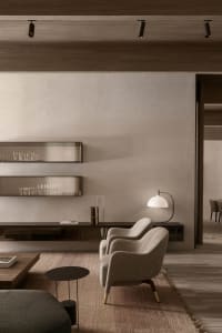 Interior of a modern minimalist living room featuring a wooden frame, grey upholstered armchair, and a natural-fiber rug.