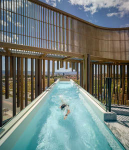 Swimmer in a modern rooftop swimming pool enclosed by glass walls.