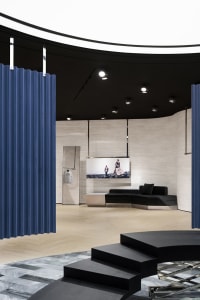 Modern pop-up store with concrete and glass materials, featuring a black sofa and blue curtains.