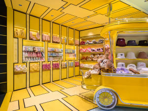 A vibrant children's toy shop with bright yellow shelves and floor, featuring various plush toys and accessories.