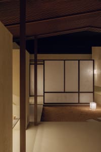 A minimalist interior featuring paper screens on wooden walls, with a small illuminated cube on the floor.