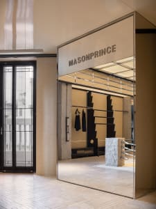 Modern retail showroom interior featuring glass storefront with clothing racks and stone pillar.