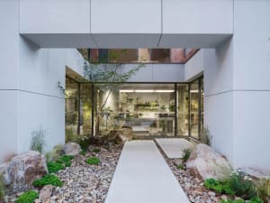 A modern office entrance featuring concrete and rock materials, with large windows and a landscaped area.