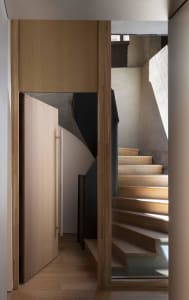 A modern interior space featuring a wooden staircase with concrete walls and sunlight.