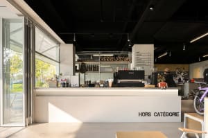 A modern coffee shop interior featuring a white counter with a menu board and a glass door.