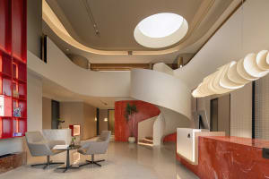 Modern office lobby interior with red marble counter, white marble chairs, concrete elements, and ambient lighting.