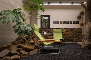 A modern patio with green folding chairs placed on a stone rock garden surrounded by plants and a stone wall.
