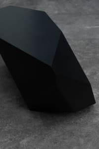 A sleek, black, metallic bench on a textured floor.