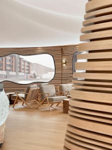 A modern hotel lobby featuring wooden walls and furniture, with a view of snowy mountains through a large window.
