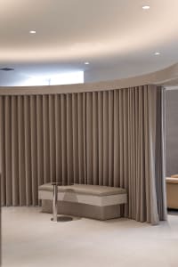 A modern minimalist spa interior featuring fabric curtains, a marble bench, and elegant lighting.