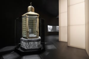 A metal exhibit display with a glass front, mounted on a marble pedestal, and topped with a golden dome.