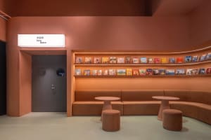 A cozy library space with brown leather seating, a bookshelf lined with various books, and two small round tables with stools