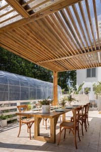Wooden dining table and chairs on a patio with a pergola overhead.