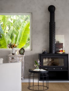 A modern living room featuring a fireplace with a black chimney, a white sofa, a small side table with a plant and a book, an