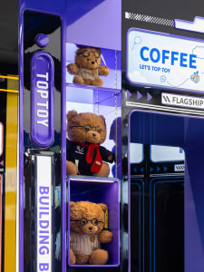 Three brown teddy bears dressed in glasses and scarves displayed in black and purple plastic shelves.