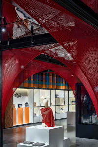 A retail store display featuring a mannequin draped in a red-netted garment, surrounded by a red-netted structure and various