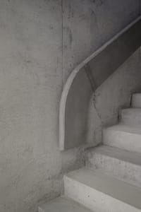 A modern, minimalist concrete staircase with smooth, curved risers against a textured concrete wall.
