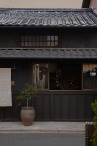 A clay pot with a plant sitting outside a building with a traditional Japanese roof design.