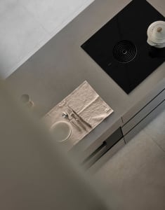 A minimalist kitchen counter featuring a concrete countertop with a plate, cutlery, and a pot, viewed from above.