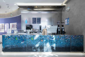 Modern coffee shop with a glass and concrete counter featuring a menu board and coffee machines.