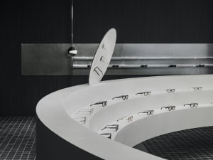 Modern white concrete walls with a curved circular display shelf showcasing black glasses.