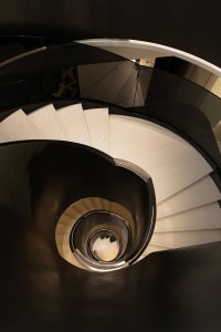 Circular glass staircase with white steps, viewed from above in a modern interior setting.