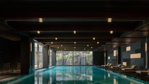 A modern swimming pool interior with concrete walls and a reflection of the ceiling lights on the water surface.