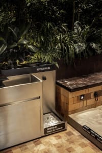 Modern public space featuring stainless steel water fountain and seating area with greenery.