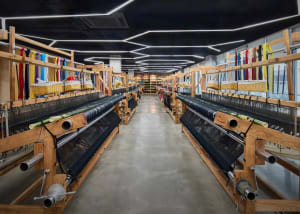 A manufacturing facility with wooden looms and colorful threads, featuring a concrete floor and modern lighting.