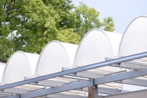 White canopy roof supported by curved metal beams with green trees in the background.