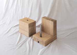 Two minimalist wooden blocks with a metal rod, placed on a white fabric background.