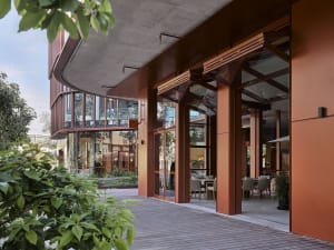 Modern restaurant entryway featuring wooden flooring, concrete structural columns, and large glass windows.