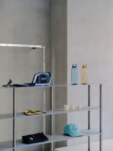 Minimalist metal shelves displaying various products, including a blue bag, colorful bottles, a yellow scarf, and a teal hat.
