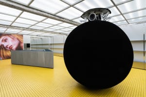 A modern installation featuring a large, metallic black sphere in a minimalistic, geometric space.