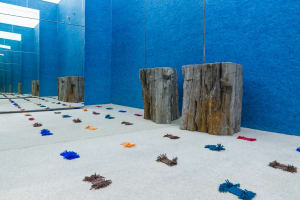 A minimalist installation featuring wooden stumps, colorful textiles, and mirrored walls.