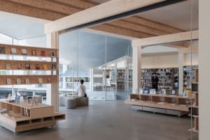 A minimalist library interior with wooden shelves, glass windows, and concrete flooring.