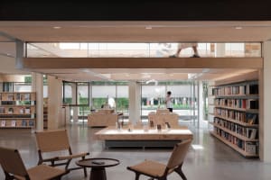A spacious modern library interior with natural lighting, wooden shelves, and minimalist furniture.