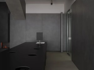 Modern, minimalist office lobby featuring concrete walls and floor, with a glass partition and lighting fixtures.