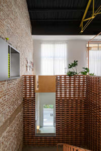 An industrial-style architectural interior with brick walls and a black beamed ceiling, featuring a brick-lined stairwell.