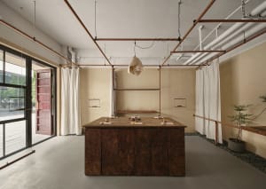 Industrial-style coffee shop interior with a rustic wooden counter, white curtains, and concrete floors.