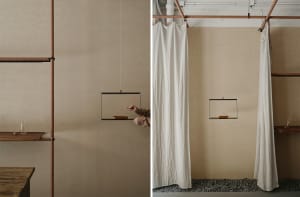 A minimalist installation featuring a white curtain hanging from a ceiling support, with a black hanging frame containing a s